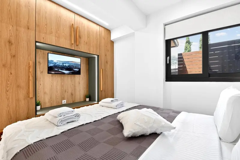 Une chambre lumineuse avec un grand lit et un mur en bois intégrant un téléviseur.