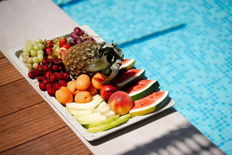 Une sélection de fruits frais est présentée sur un plat blanc au bord d'une piscine.