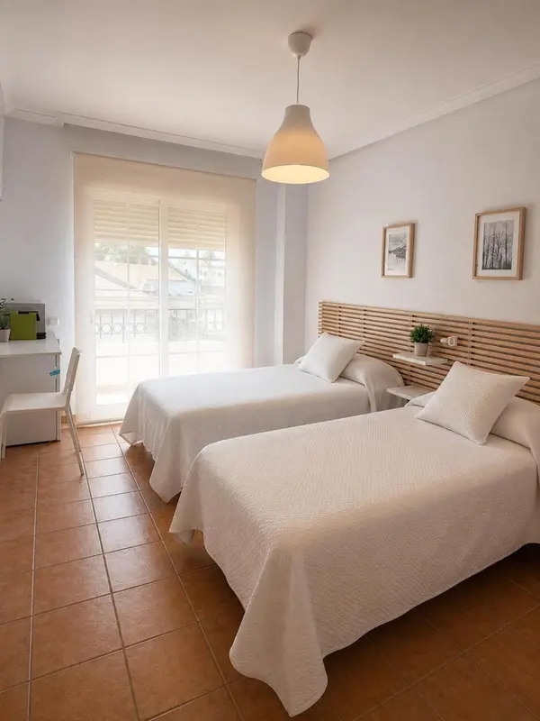 Une chambre lumineuse avec deux lits simples et un bureau près d'une fenêtre.
