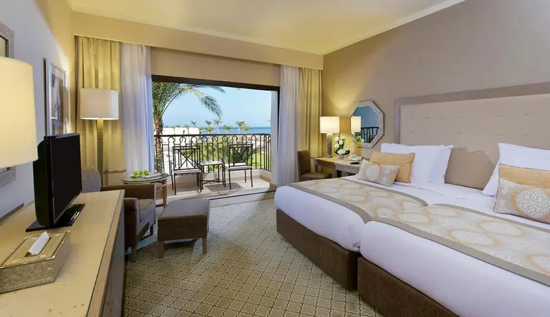 Chambre lumineuse avec un grand lit et une vue sur la mer depuis un balcon.