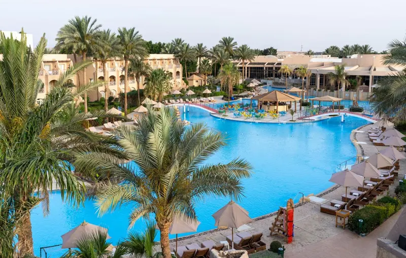 Vue aérienne d'une grande piscine d'hôtel entourée de palmiers et de transats.