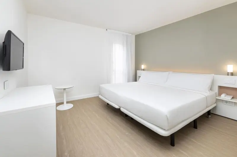 Une chambre lumineuse avec un grand lit et un téléviseur mural.