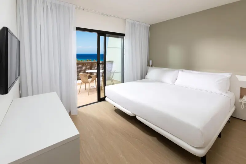 Une chambre lumineuse avec un grand lit et un balcon donnant sur la mer.