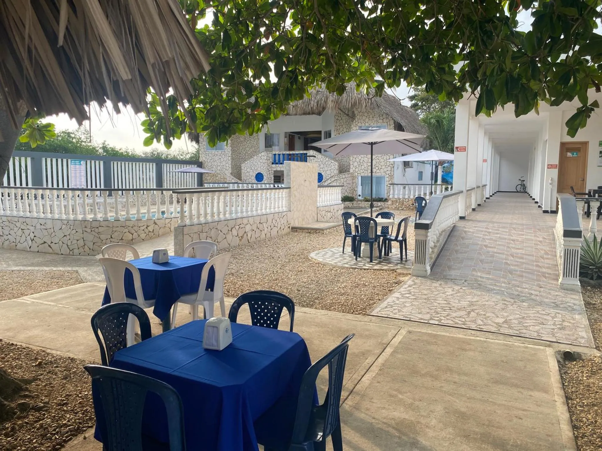 Tables et chaises bleues disposées sur une terrasse gravillonnée devant un bâtiment blanc.