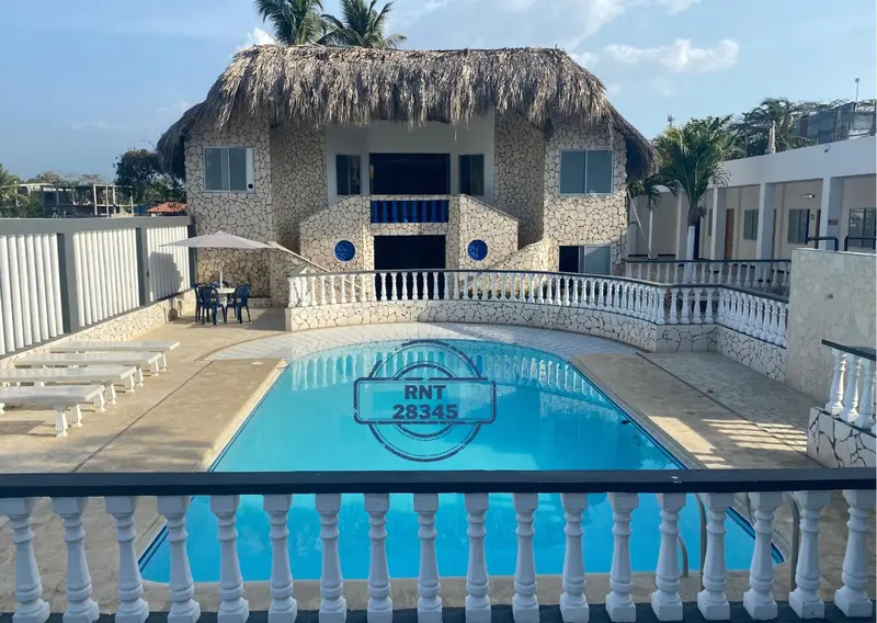 Bâtiment blanc avec toiture de chaume surplombant une piscine turquoise.