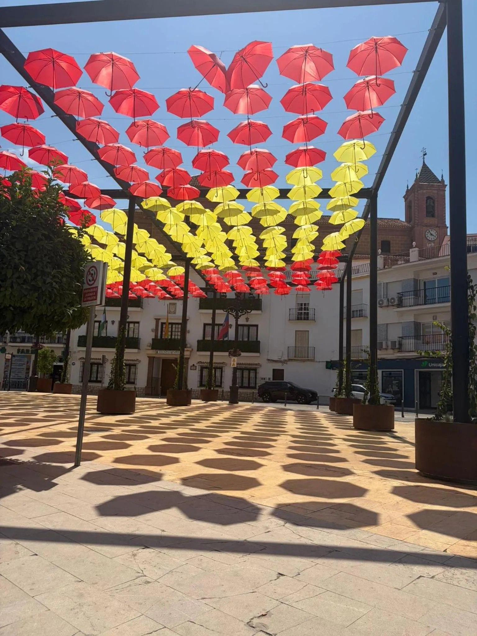 Une place ombragée par des parasols colorés suspendus au-dessus d'une surface pavée.