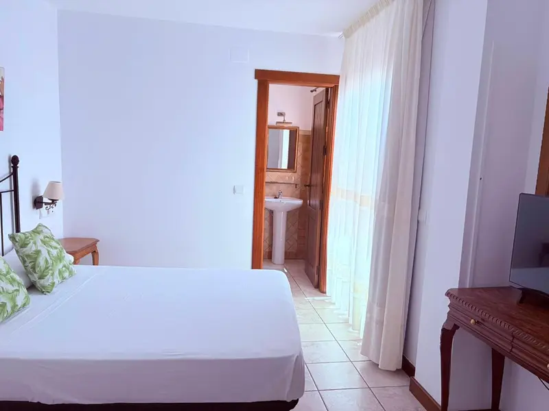 Une chambre lumineuse avec un lit blanc et un accès à une salle de bain.