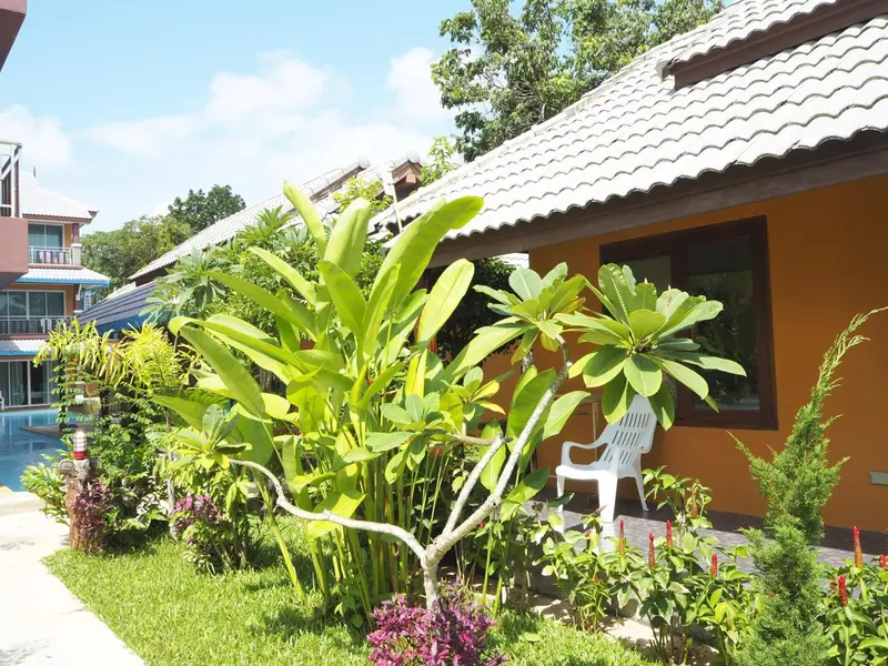 Façade d'un bâtiment aux tuiles grises et aux murs orange, entouré de végétation tropicale.