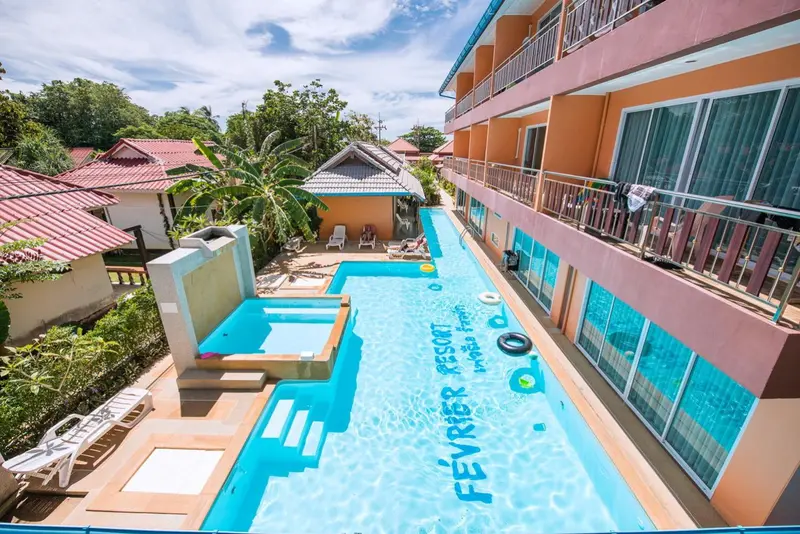 Vue aérienne d'une piscine turquoise bordée de bâtiments colorés et de végétation tropicale.