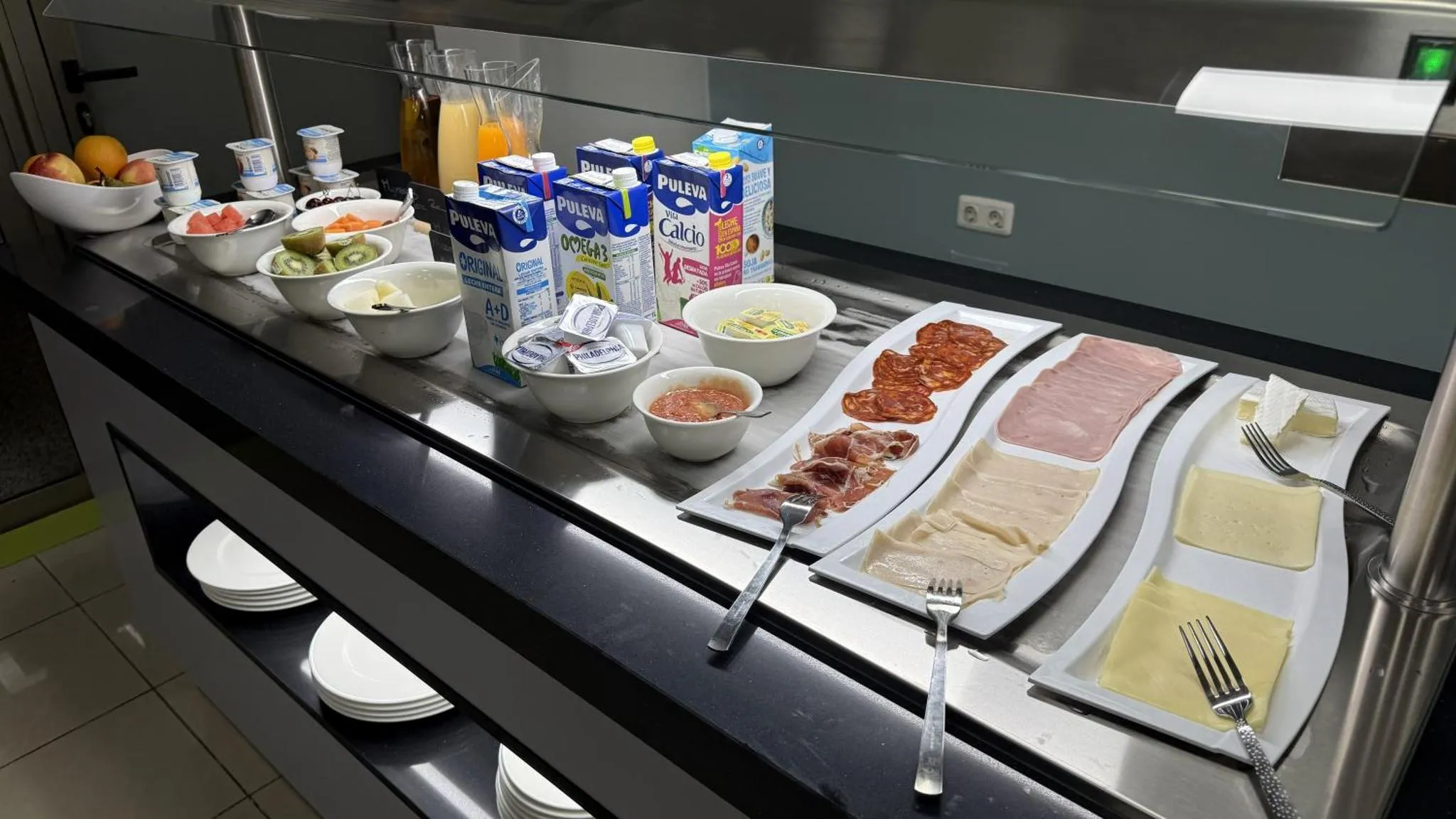 Un buffet propose des viennoiseries, des fruits, des boissons et de la charcuterie.