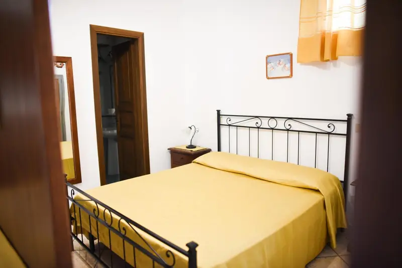 Une chambre avec un lit recouvert d'une couverture jaune et un miroir mural.
