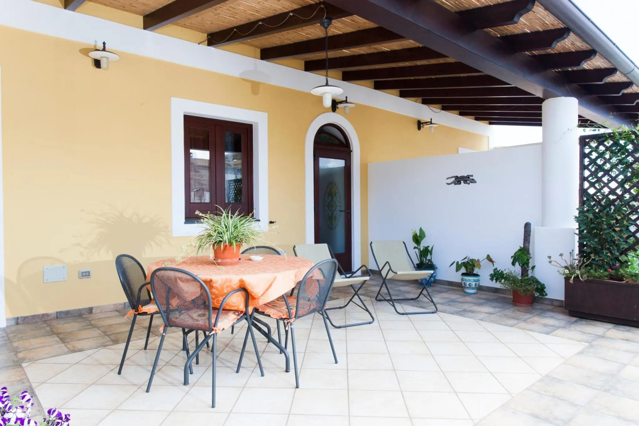 Une table à manger est placée sur une terrasse carrelée ombragée.
