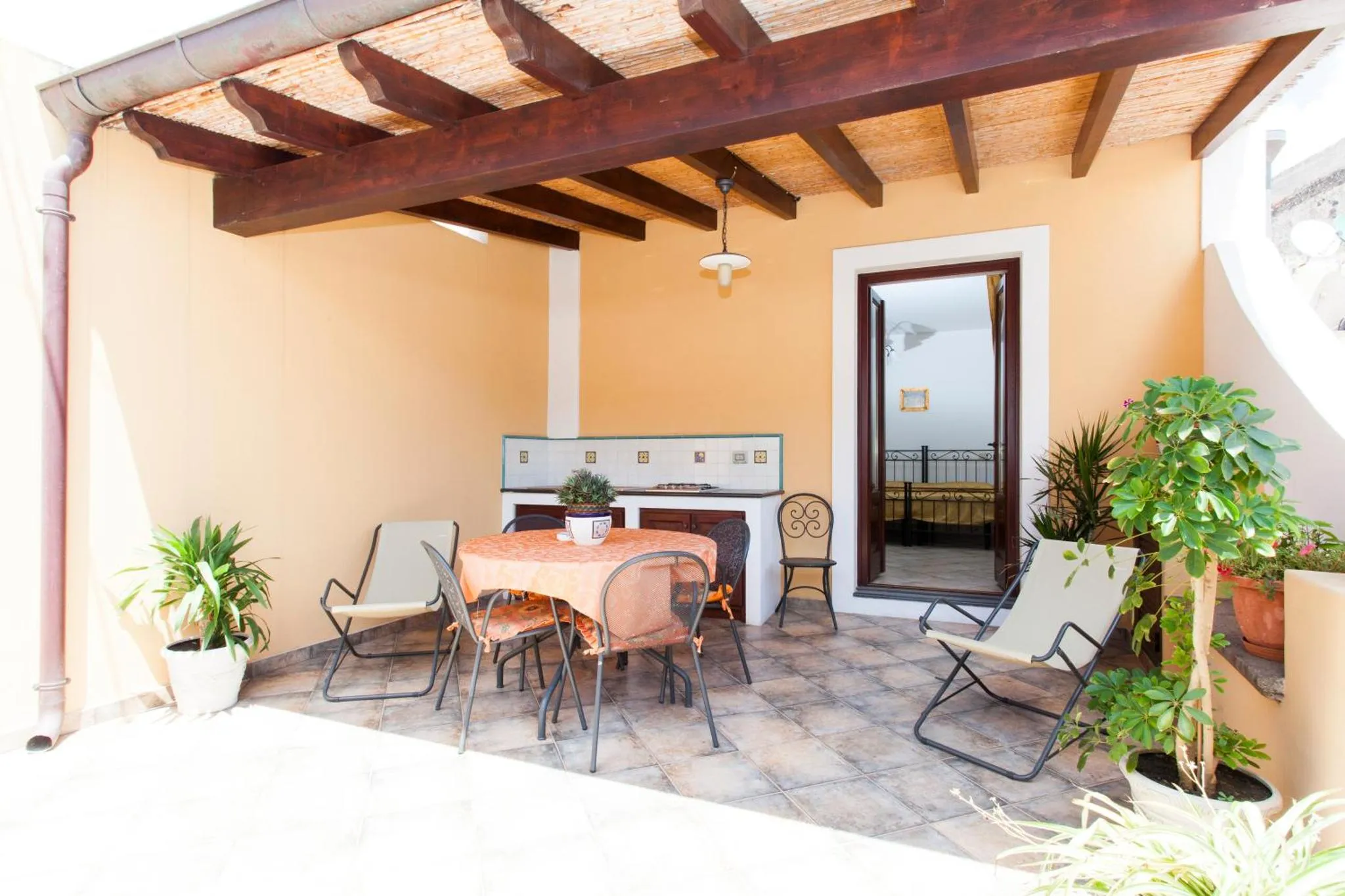 Terrasse ombragée avec table et chaises, donnant sur une chambre.