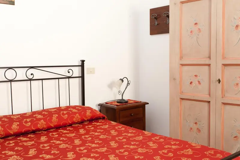 Une chambre avec un lit recouvert d'une courtepointe rouge et une commode en bois.