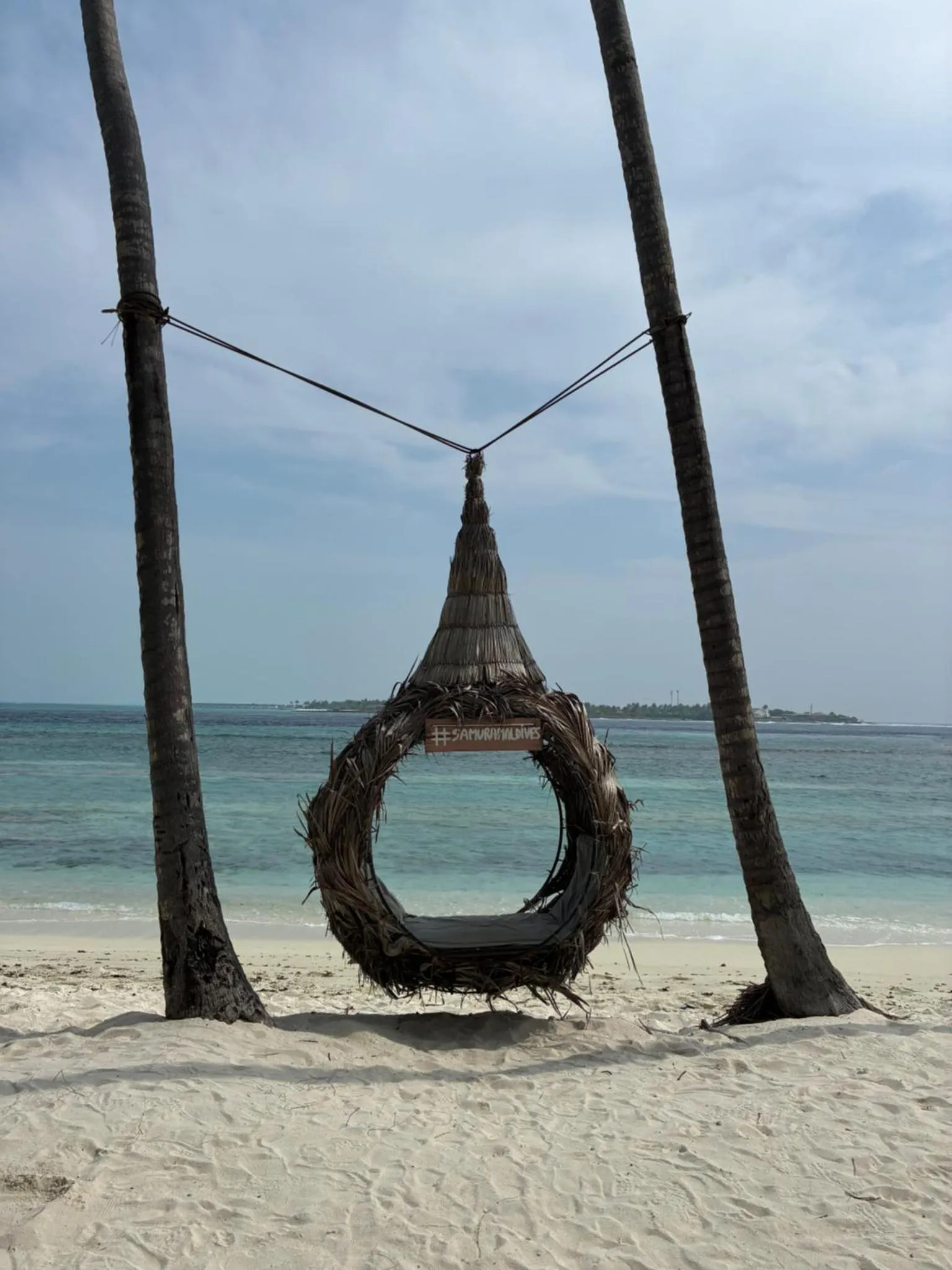 Un hamac tisse suspendu entre deux palmiers sur une plage de sable blanc.