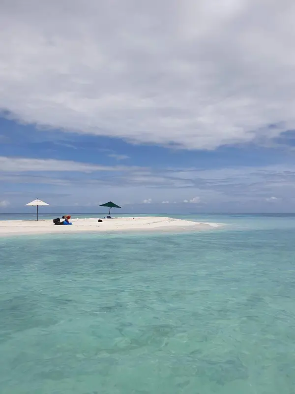 Plage de sable blanc avec parasols et eau turquoise sous un ciel bleu.