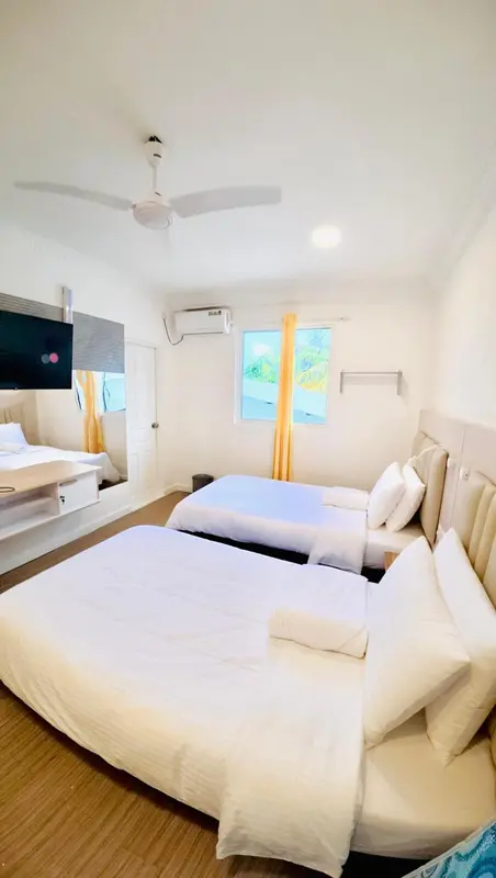Une chambre lumineuse avec deux lits simples et un ventilateur au plafond.