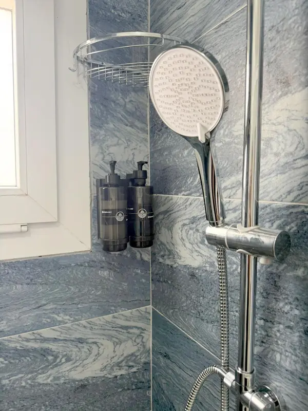 Une douche à l'italienne avec pommeau chromé et étagère murale.