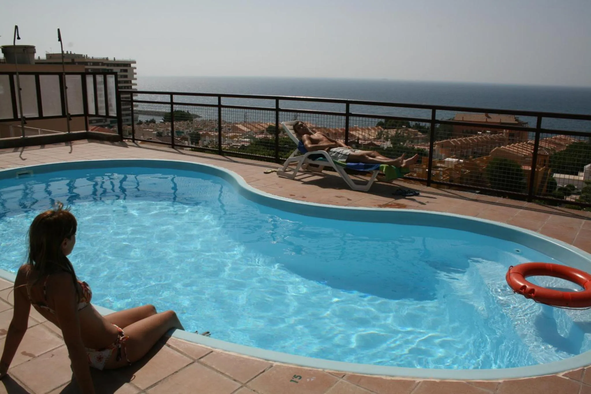 Une piscine sur une terrasse avec des personnes se relaxant au soleil.