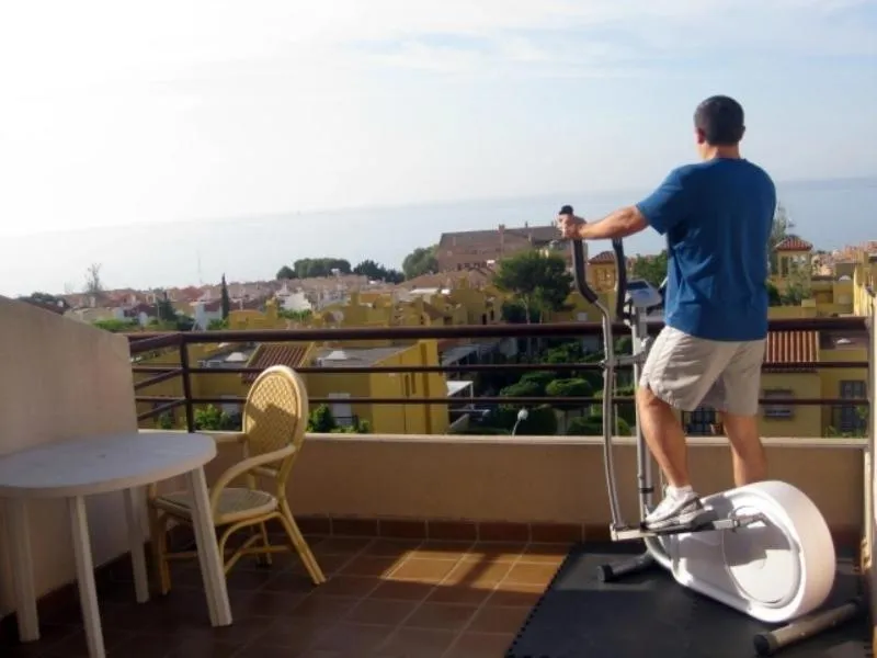 Un homme fait de l'exercice sur un appareil elliptique sur une terrasse avec vue sur la mer.