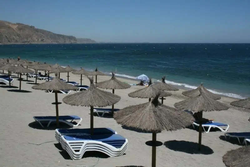 Transats et parasols sur une plage de sable fin bordée par une mer bleue.