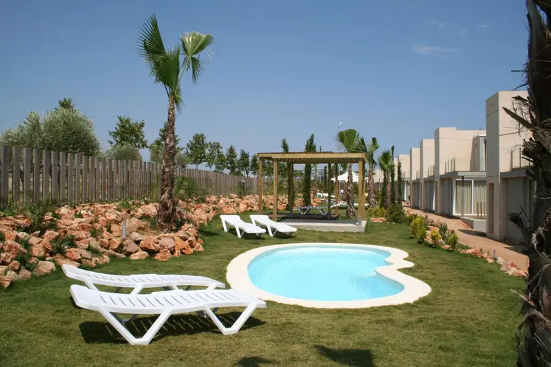 Transats blancs disposés autour d'une petite piscine dans un jardin soigné.