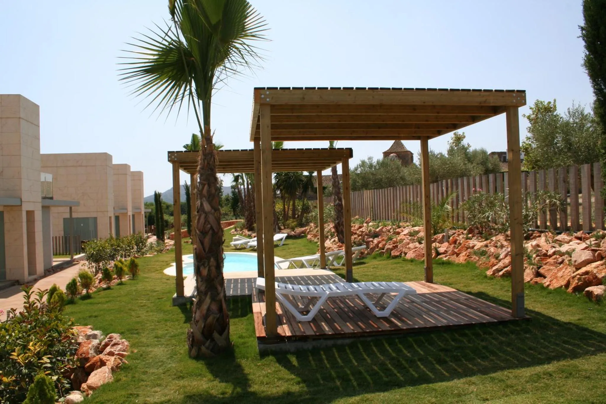 Terrasse en bois avec transats près d'une piscine dans un jardin soigné.