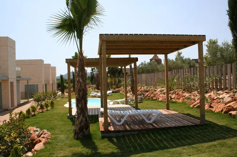 Terrasse en bois avec transats près d'une piscine dans un jardin soigné.