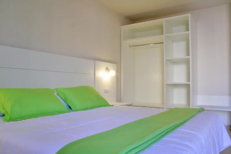 Une chambre lumineuse avec un lit recouvert d'une couverture verte et un grand placard intégré.