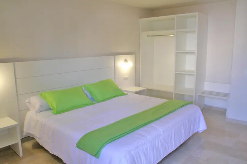 Une chambre lumineuse avec un grand lit recouvert d'une couette verte.