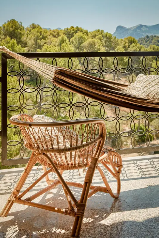 Un hamac et un fauteuil en rotin sur une terrasse ensoleillée.
