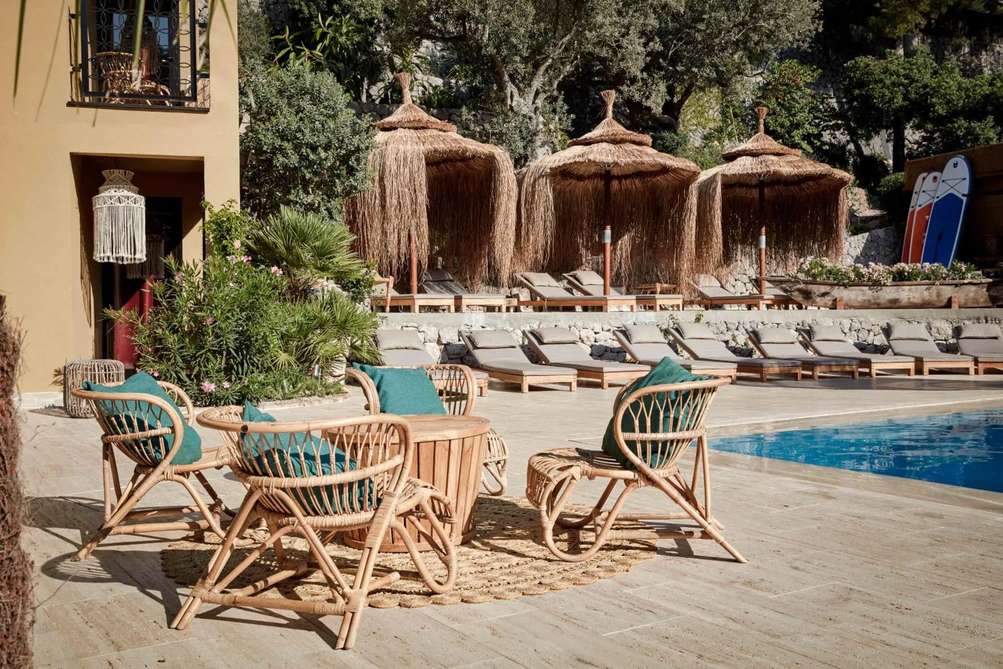 Espace de détente extérieur avec mobilier en rotin et parasols en chaume près d'une piscine.