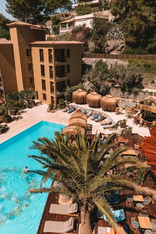 Vue aérienne d'une piscine turquoise entourée de transats et de palmiers.