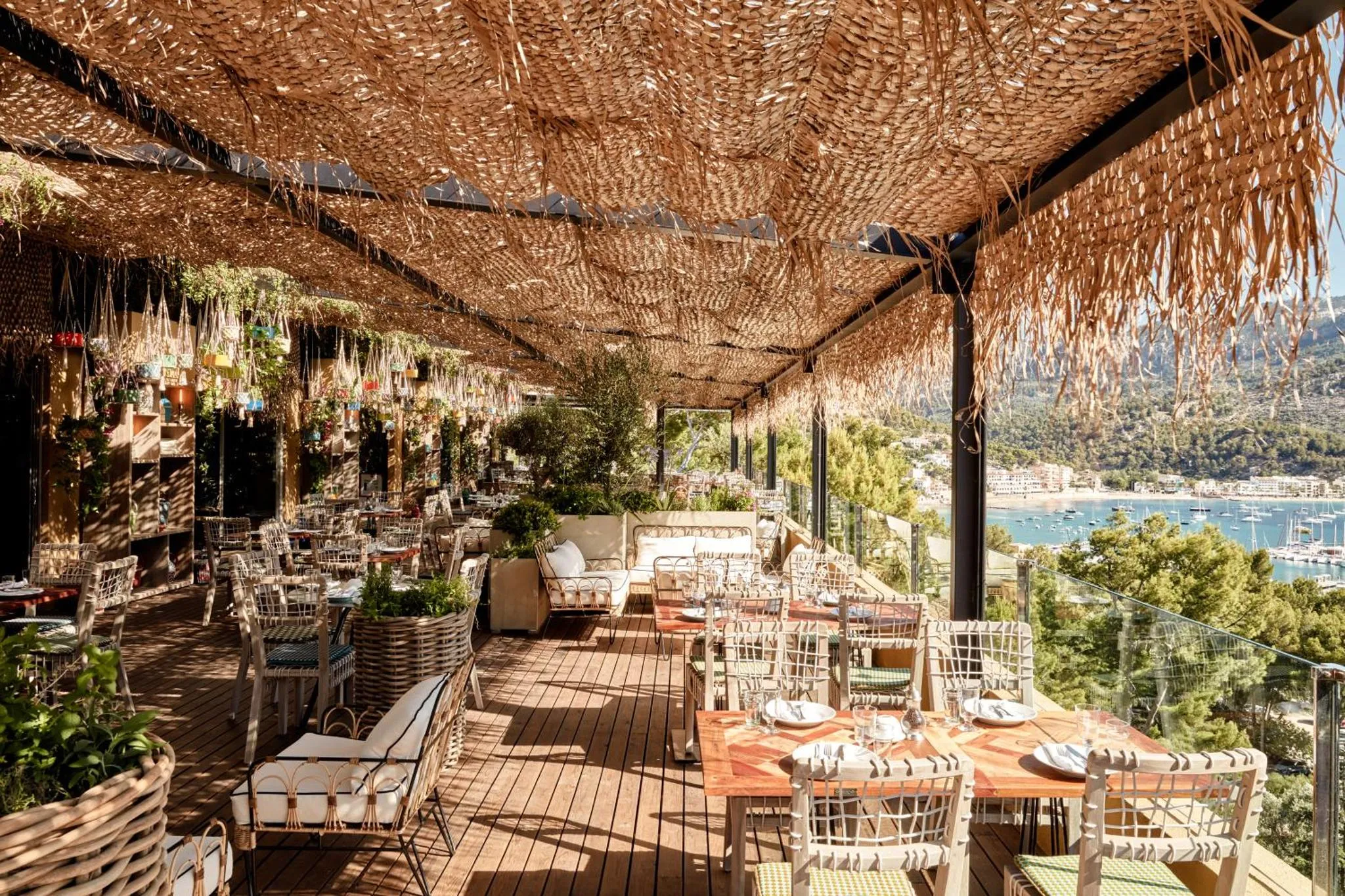 Terrasse ombragée avec tables et chaises donnant sur la mer.