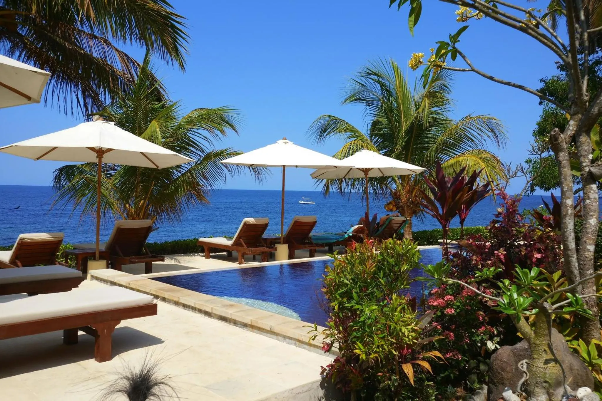 Transats et parasols bordent une piscine à débordement avec vue sur la mer.