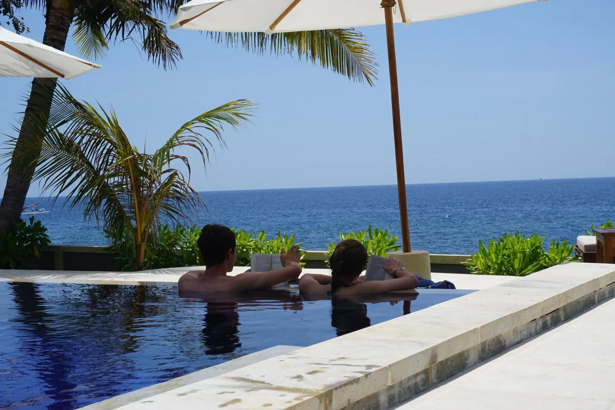 Deux personnes se détendent dans une piscine avec vue sur la mer.