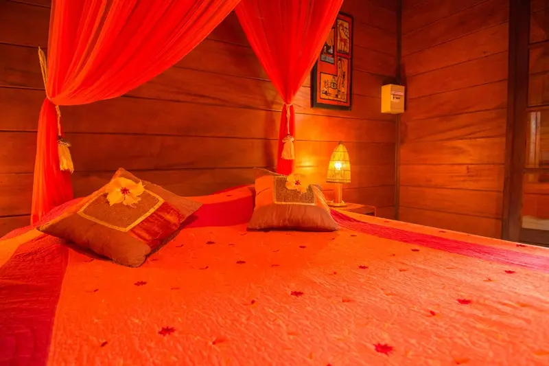 Lit recouvert d'un tissu rouge vif dans une chambre aux murs en bois.