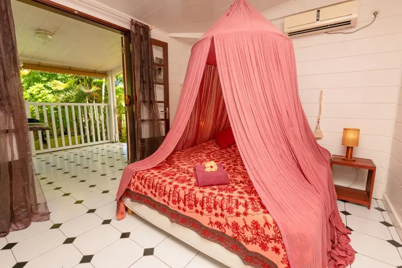 Une chambre avec un lit à baldaquin rose et une vue sur une terrasse.