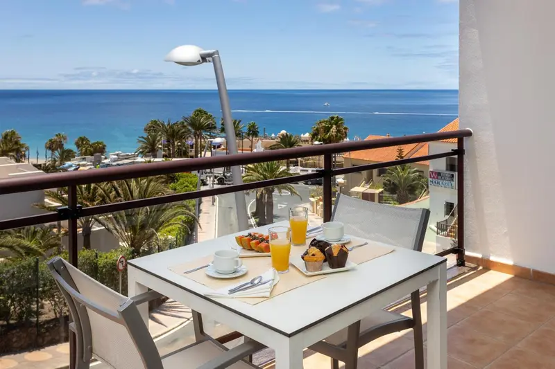 Une table de petit-déjeuner est dressée sur un balcon avec vue sur la mer.