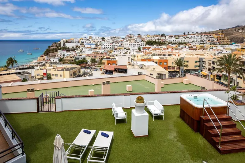 Terrasse aménagée avec jacuzzi et chaises longues surplombant une ville côtière.