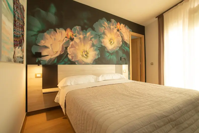 Une chambre lumineuse avec un grand lit et un mur décoré de fleurs.