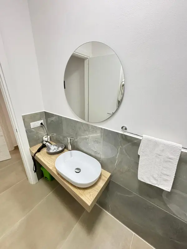 Un lavabo blanc sur un meuble en bois clair, devant un miroir rond.