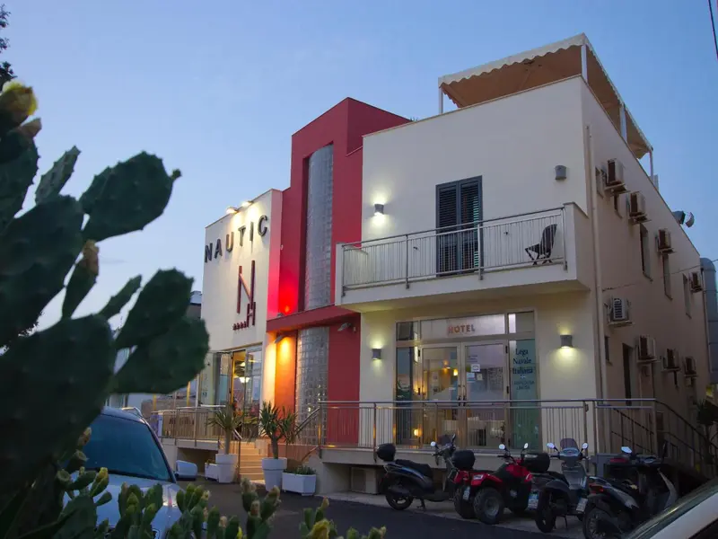 Façade d'un bâtiment moderne avec un éclairage nocturne et une végétation tropicale.