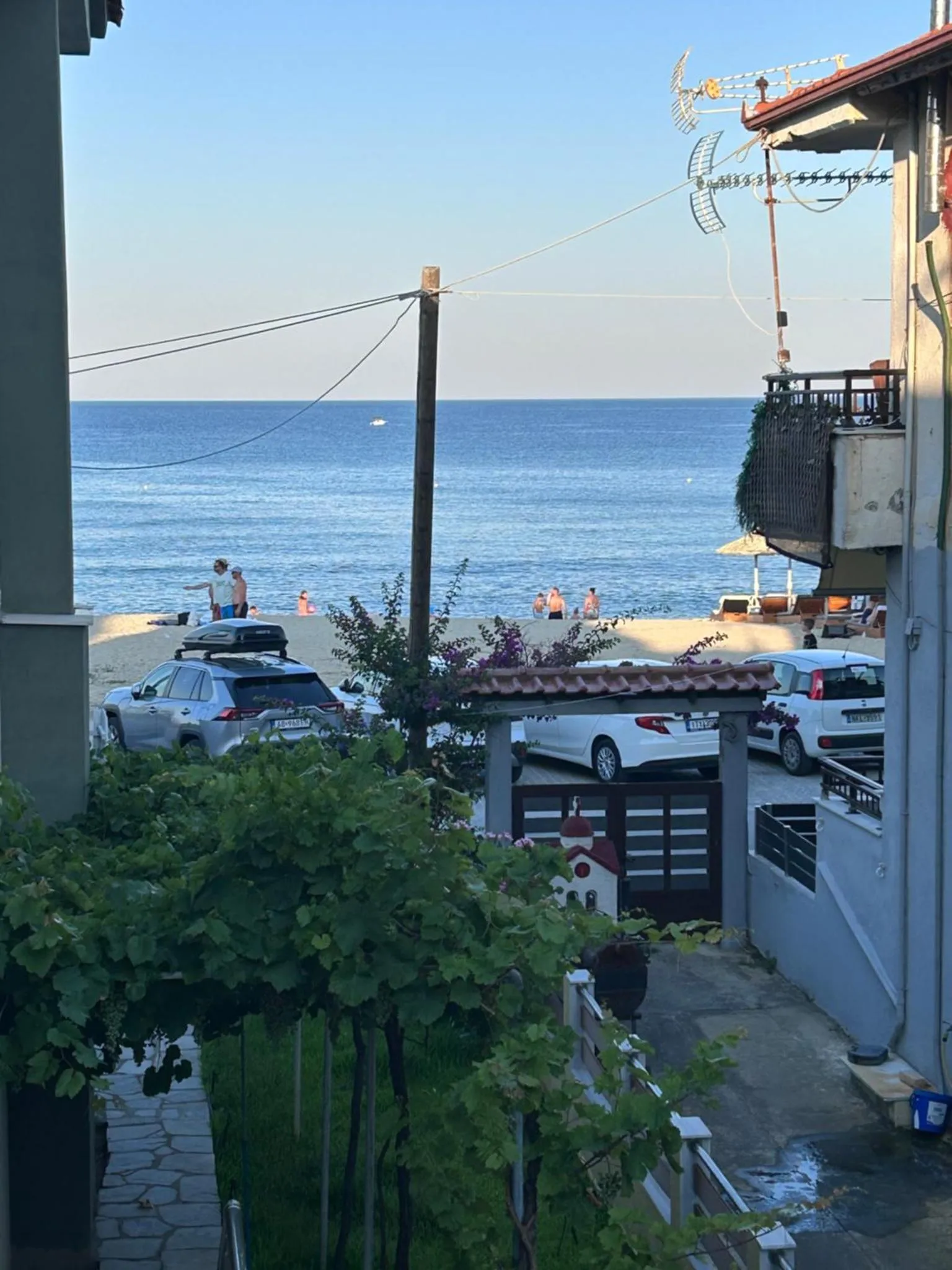 Vue sur la mer depuis un balcon fleuri avec des véhicules garés en contrebas.