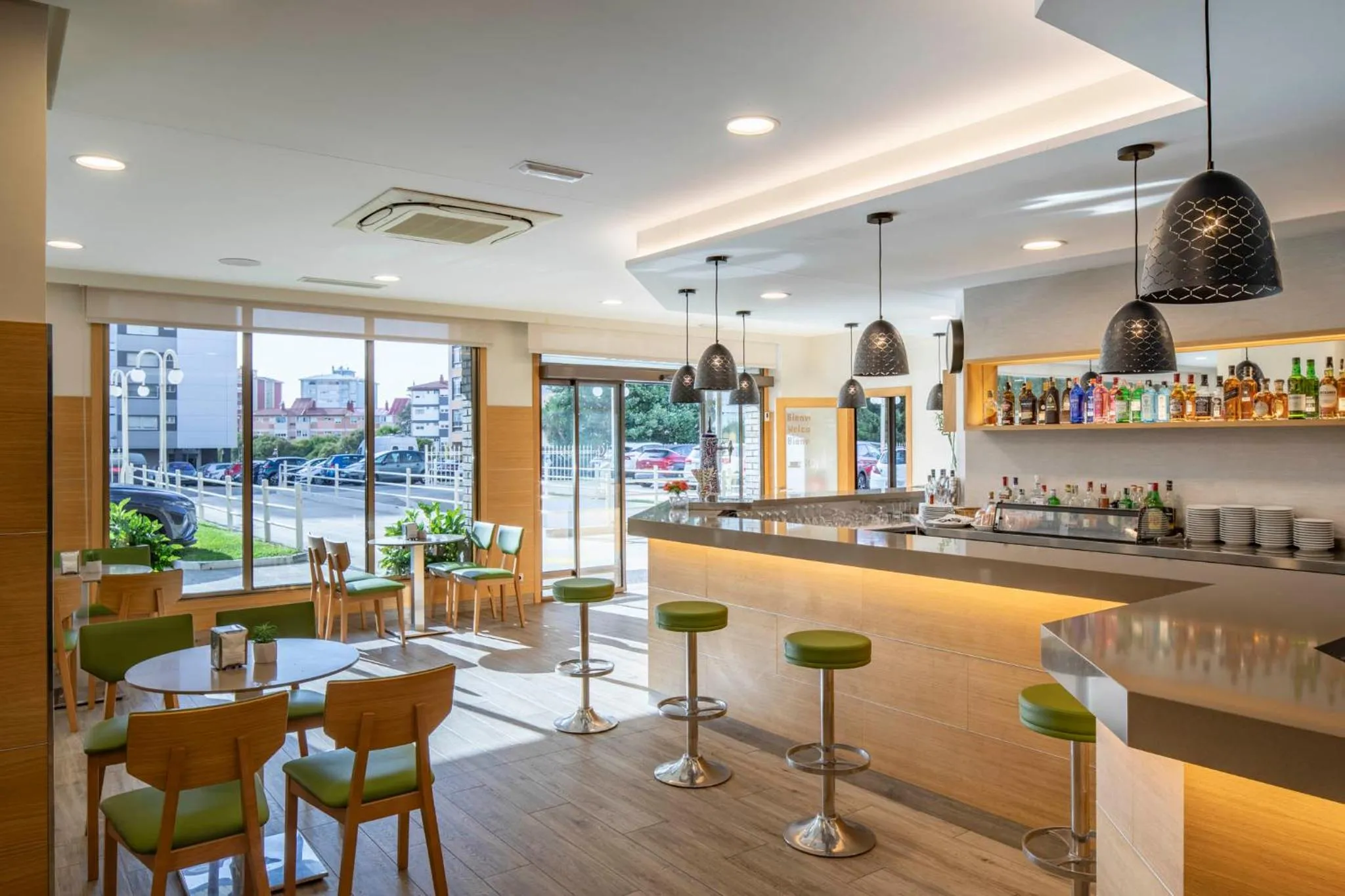 Un bar lumineux avec un comptoir en bois et des tabourets verts, donnant sur une vue extérieure.