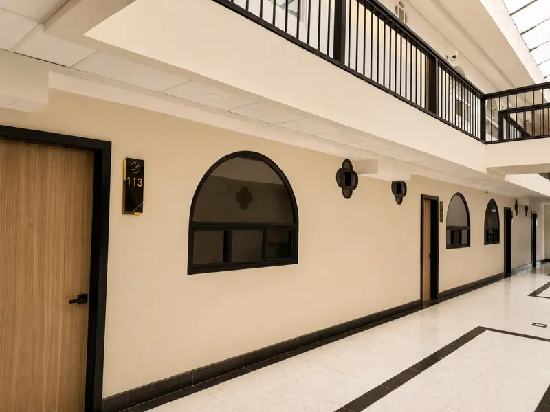 Un couloir d'hôtel avec une porte numérotée et des ouvertures décoratives.