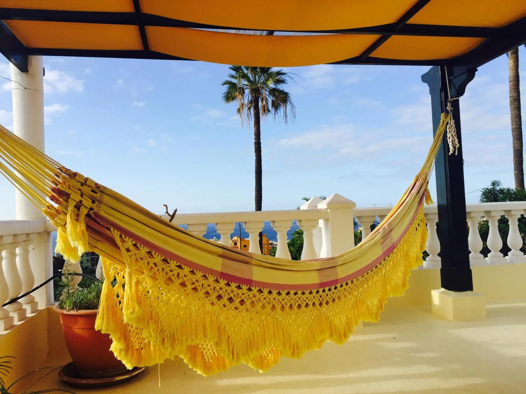 Un hamac coloré est suspendu sur une terrasse ensoleillée avec vue sur la mer.