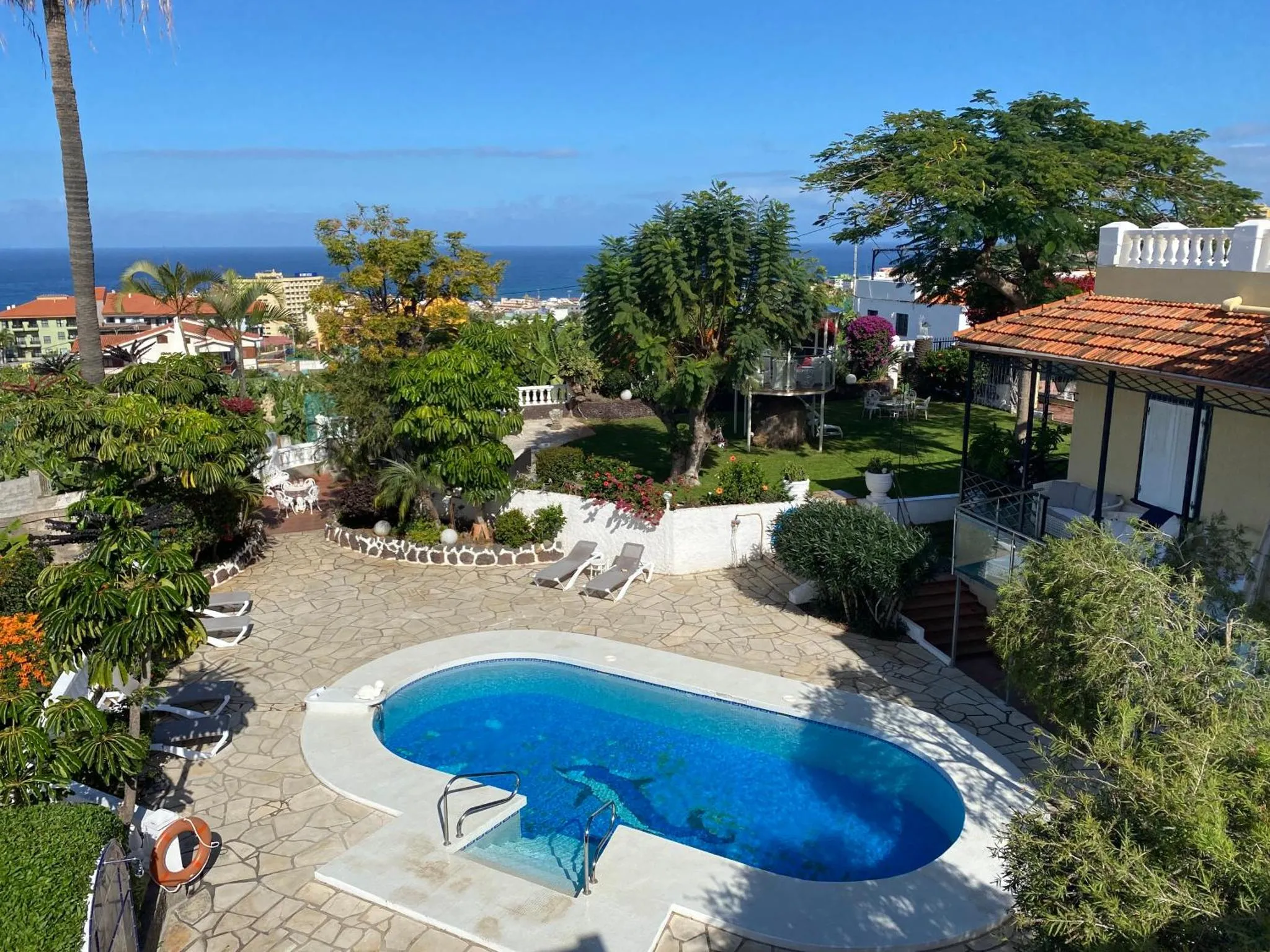 Vue aérienne d'une piscine au sein d'un jardin luxuriant avec vue sur la mer.