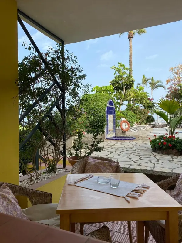 Une table est dressée sur une terrasse ensoleillée avec vue sur une végétation luxuriante.