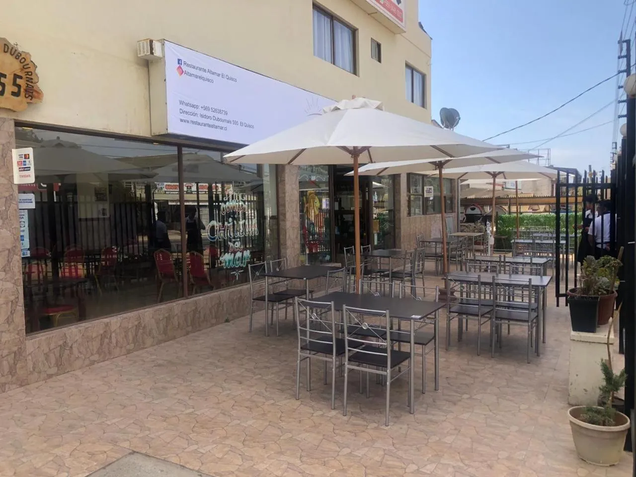Terrasse ombragée avec tables et chaises devant un bâtiment.